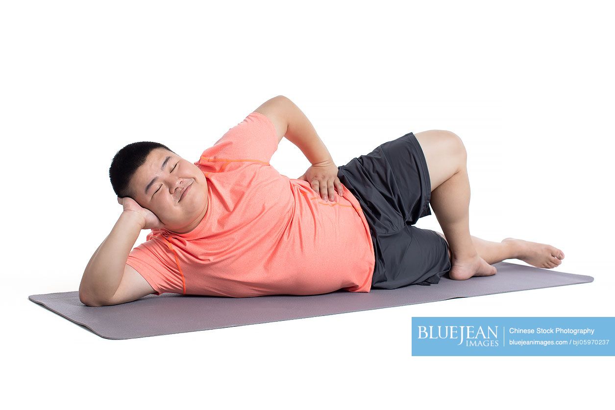 Overweight young Chinese man lying on exercise mat
