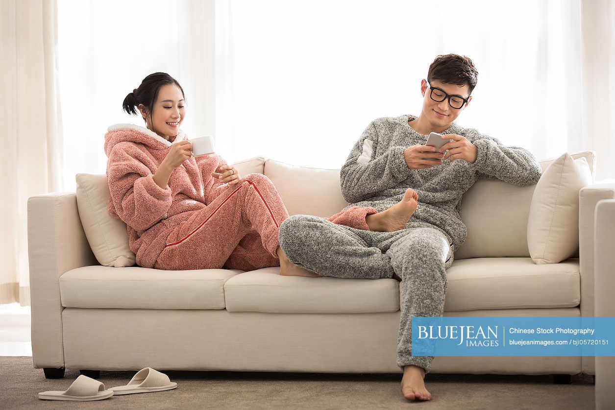 Happy young Chinese couple relaxing on sofa