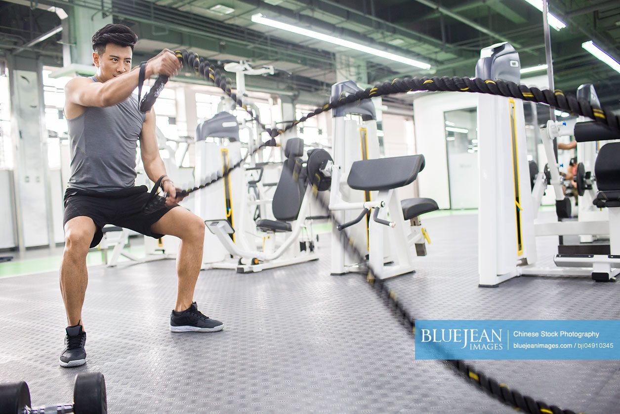 Young Chinese man exercising with battling rope at gym