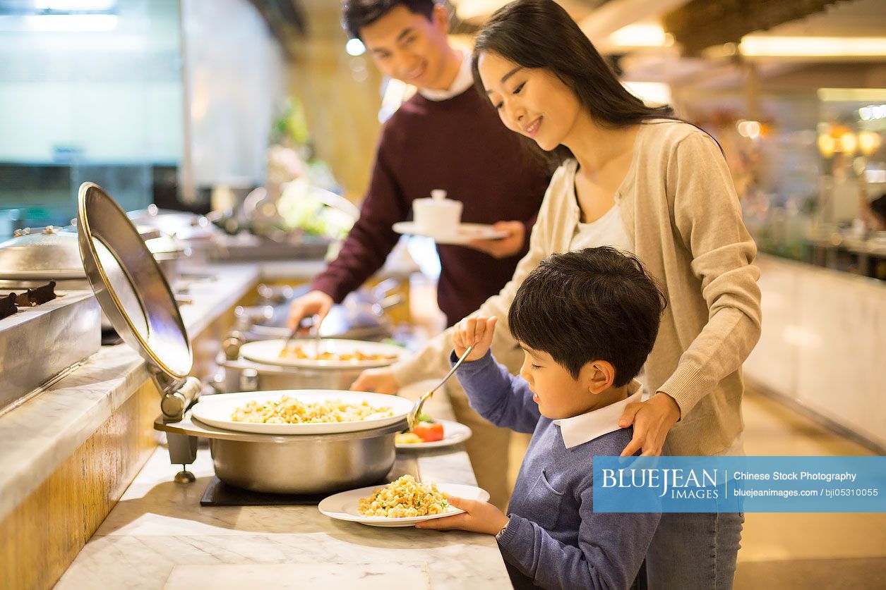 Cheerful young Chinese family taking food from buffet table