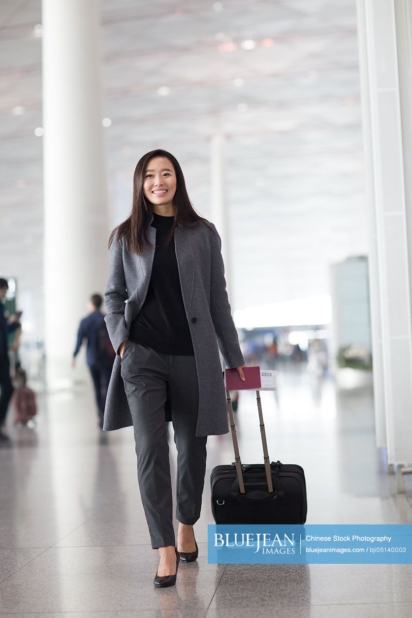 Chinese businesswoman pulling wheeled luggage in airport lobby