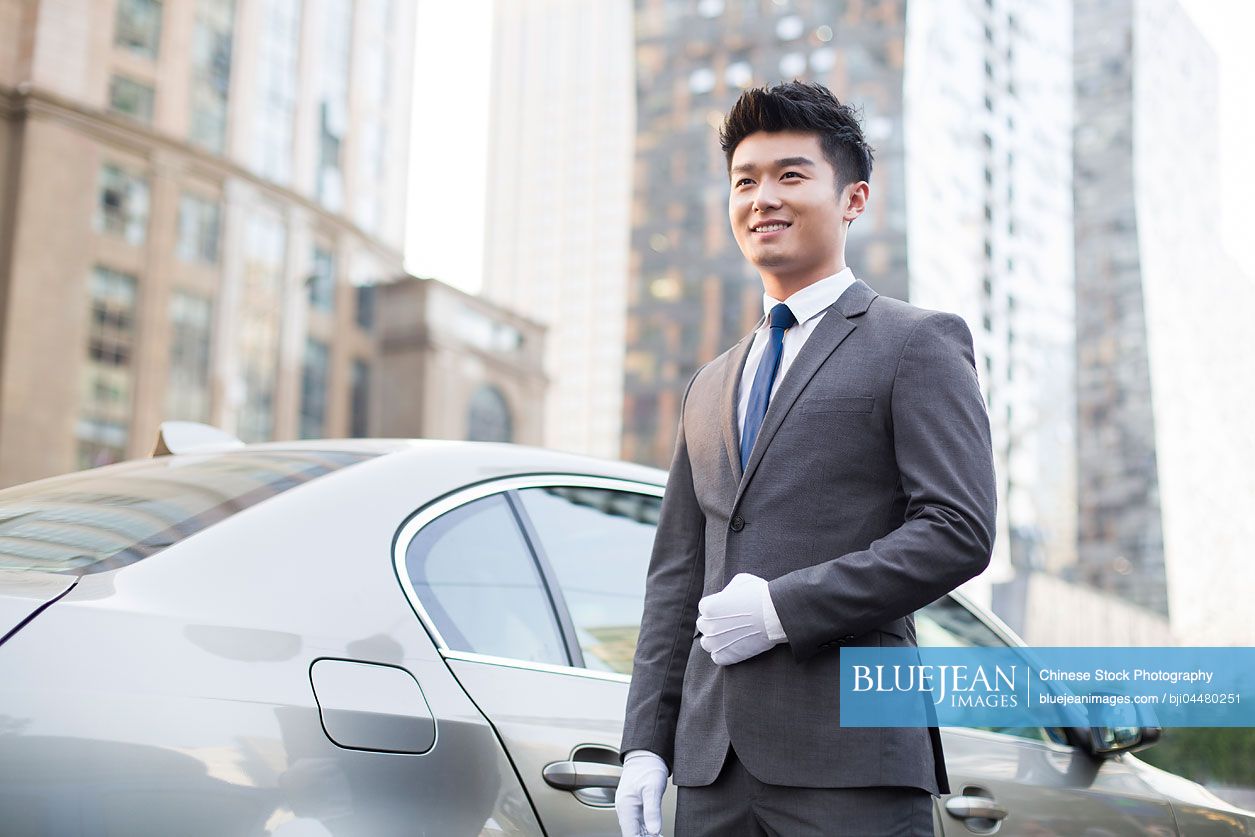Chinese chauffeur standing next to the car