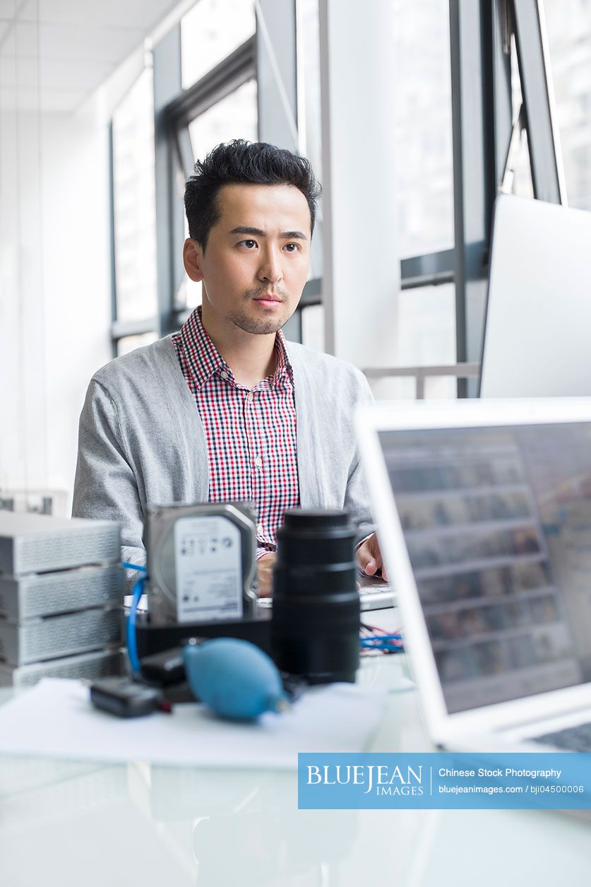 Male Chinese photographer working in office with computer