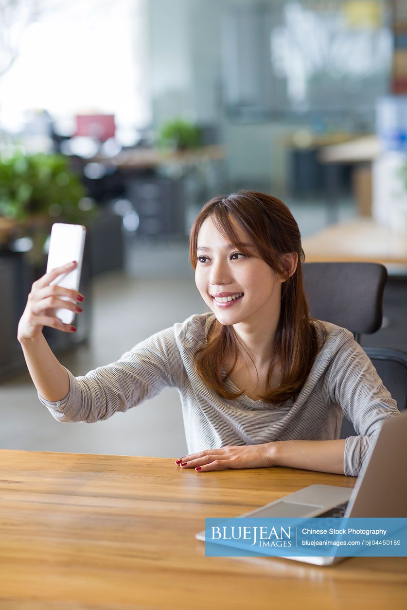 Young Chinese woman taking self portrait in office