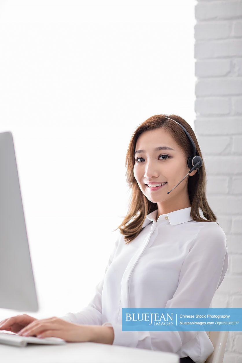 Cheerful young Chinese businesswoman with headset in office