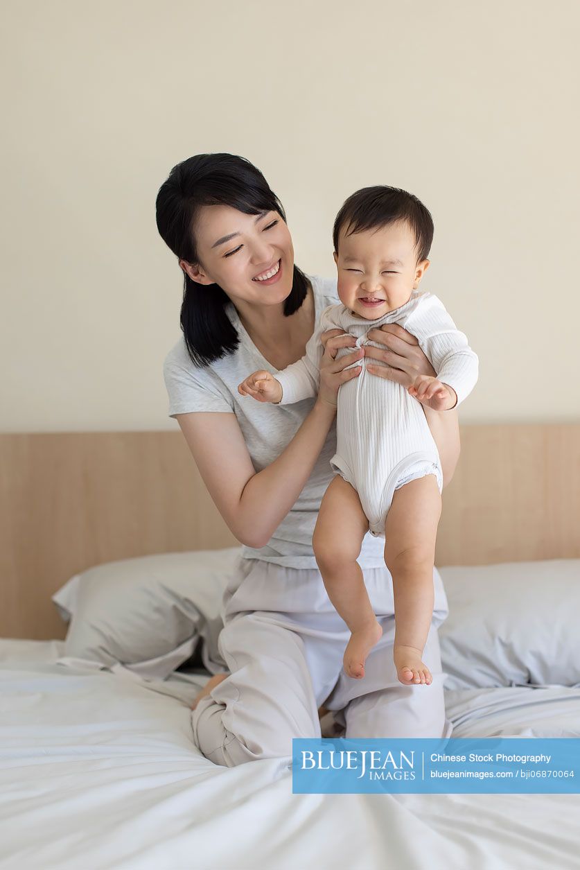Cheerful young Chinese mother playing with baby