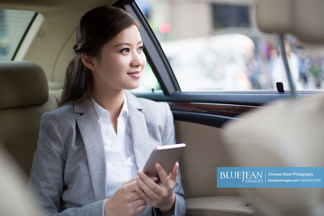 Chinese businesswoman holding smart phone in car back seat