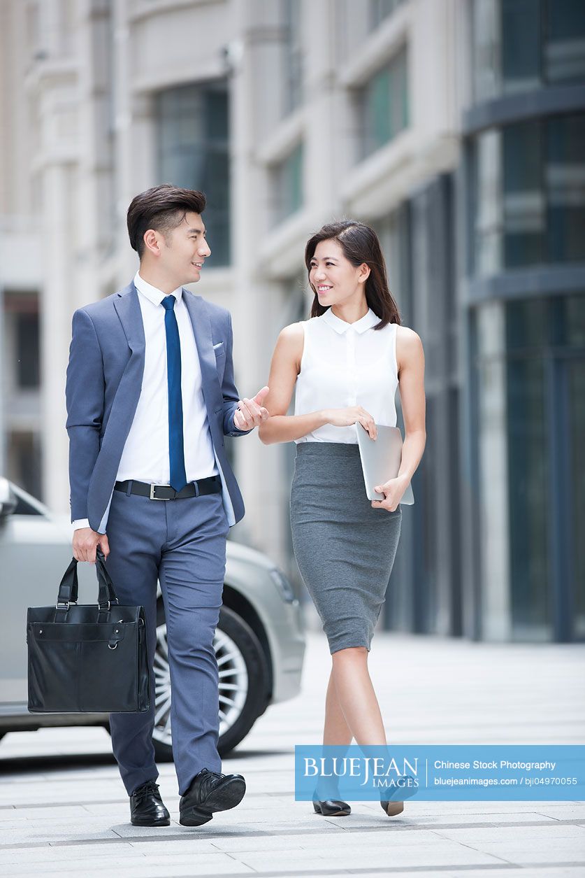 Confident Chinese business people talking and walking outdoors