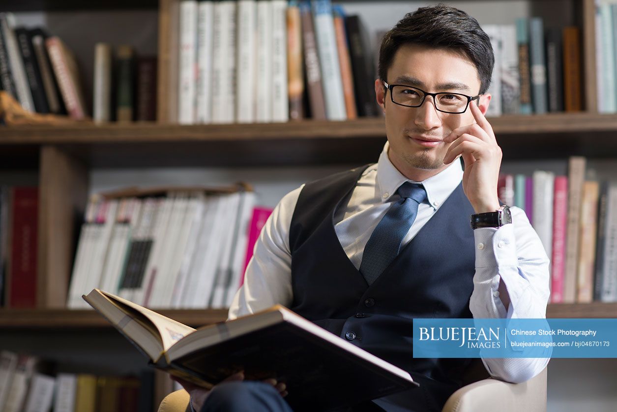 Young Chinese businessman reading book in his study