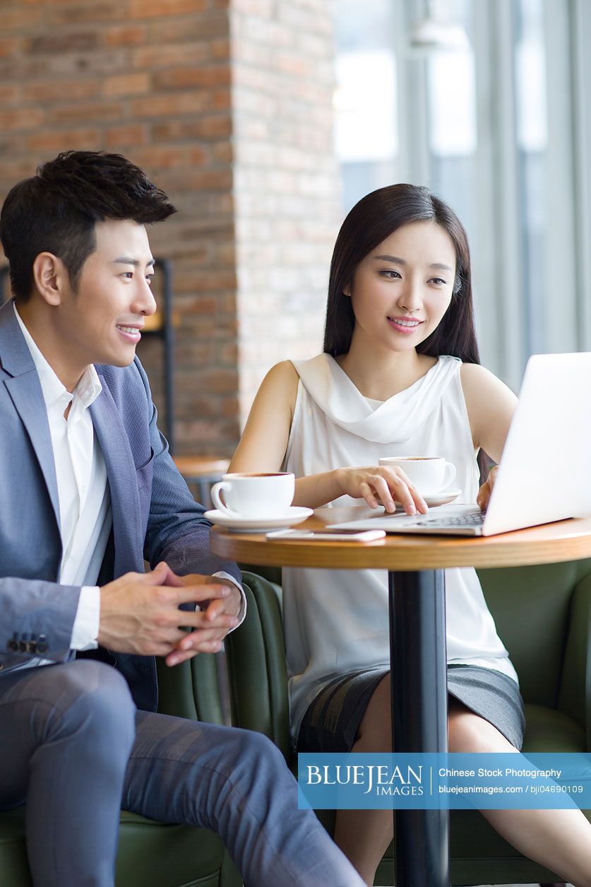 Chinese businesswoman and businessman working with laptop in café
