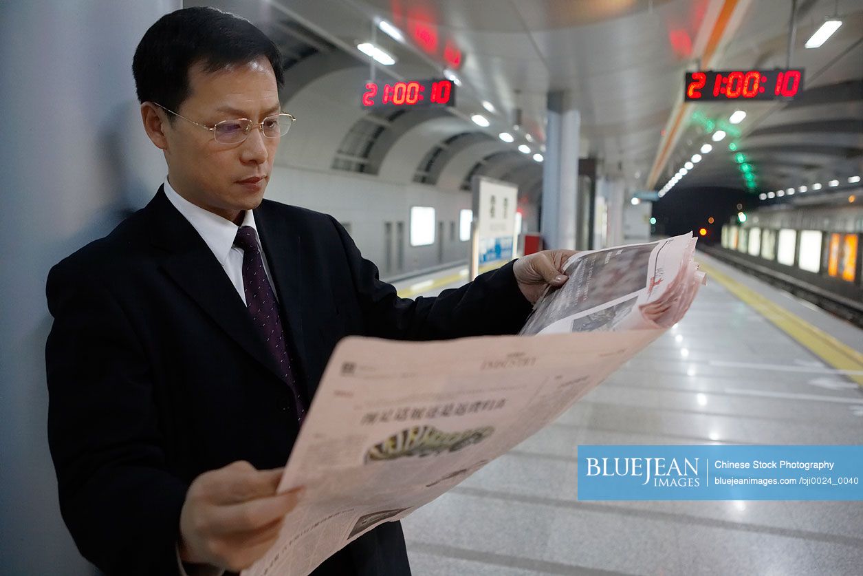 Chinese businessman reading newspaper in train station