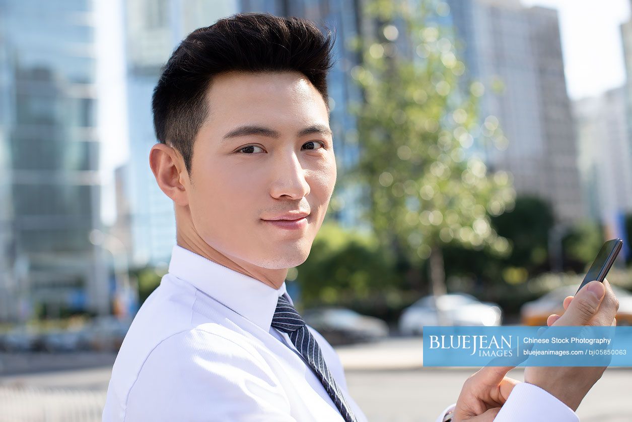 Confident young Chinese businessman using smart phone