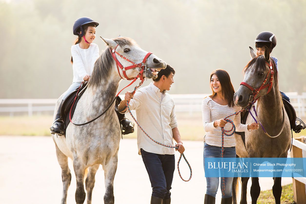 Cheerful young Chinese family riding horses