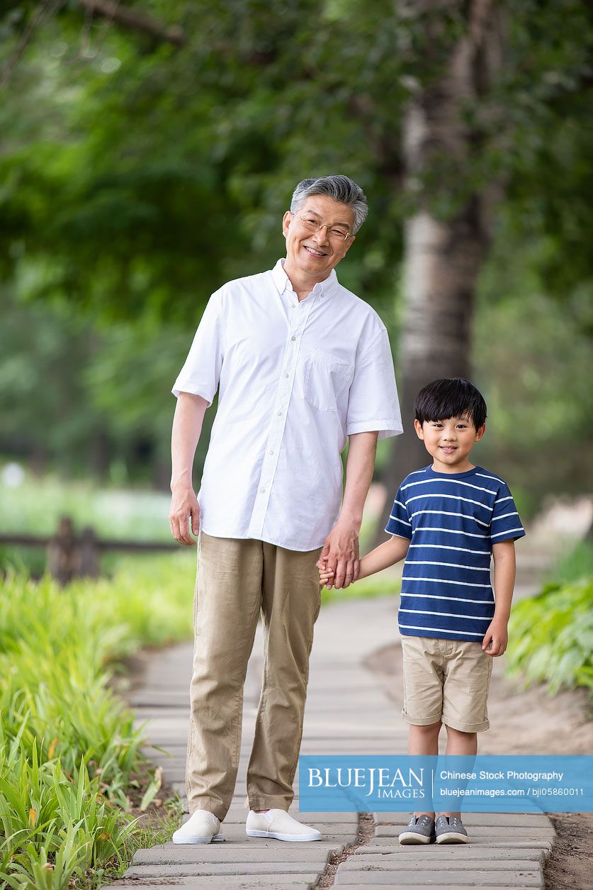 Happy Chinese grandfather and grandson holding hands in park