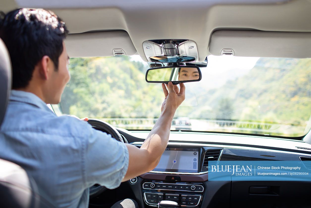 Young Chinese man adjusting rear-view mirror in car