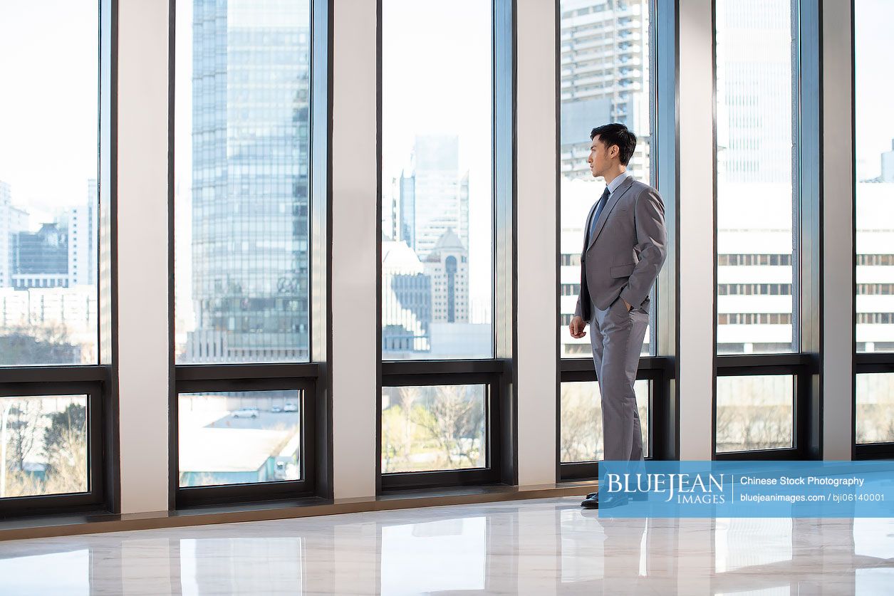 Young Chinese businessman looking through window