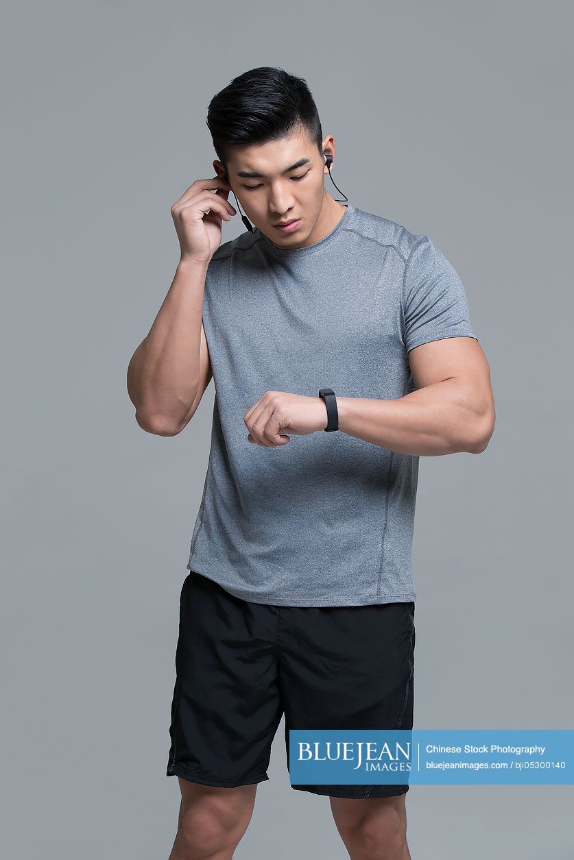 Young chinese male athlete with headphones checking smart watch after
