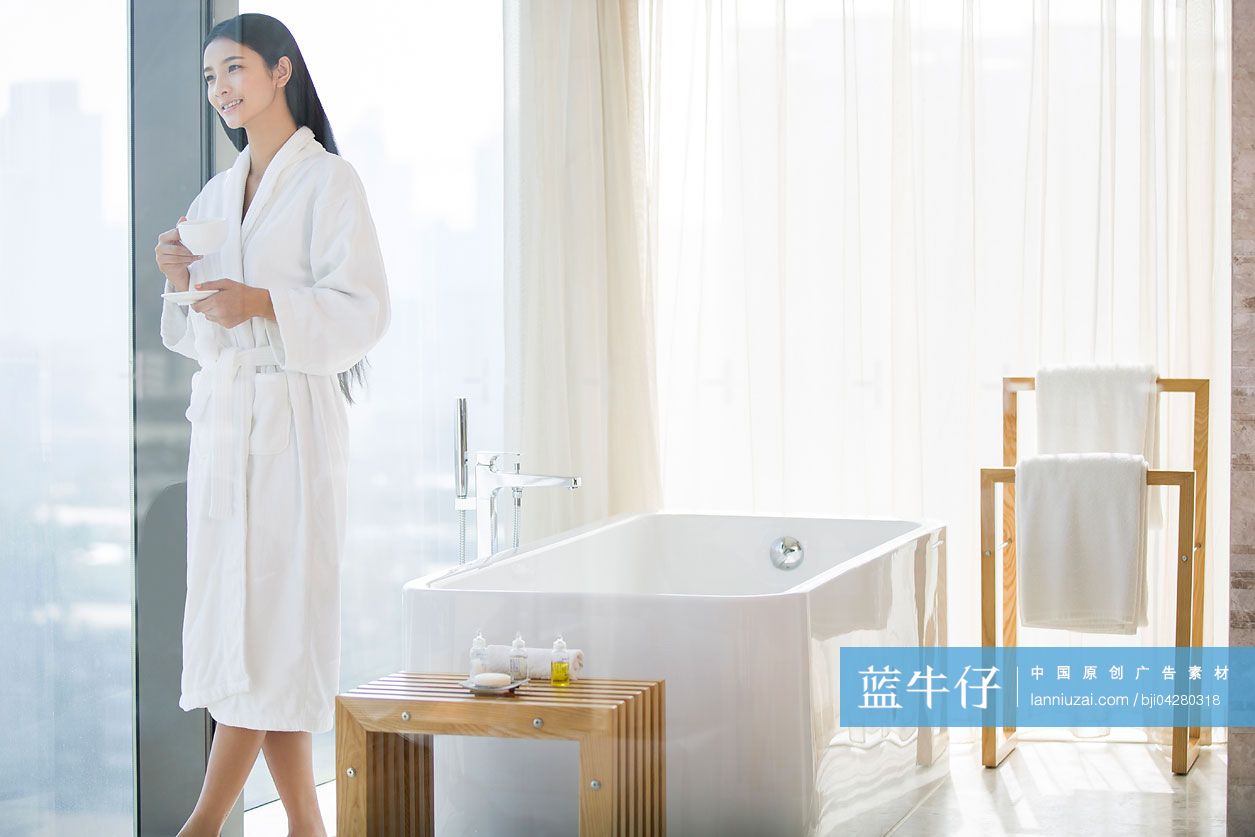 穿着浴袍的女子站在窗边喝咖啡