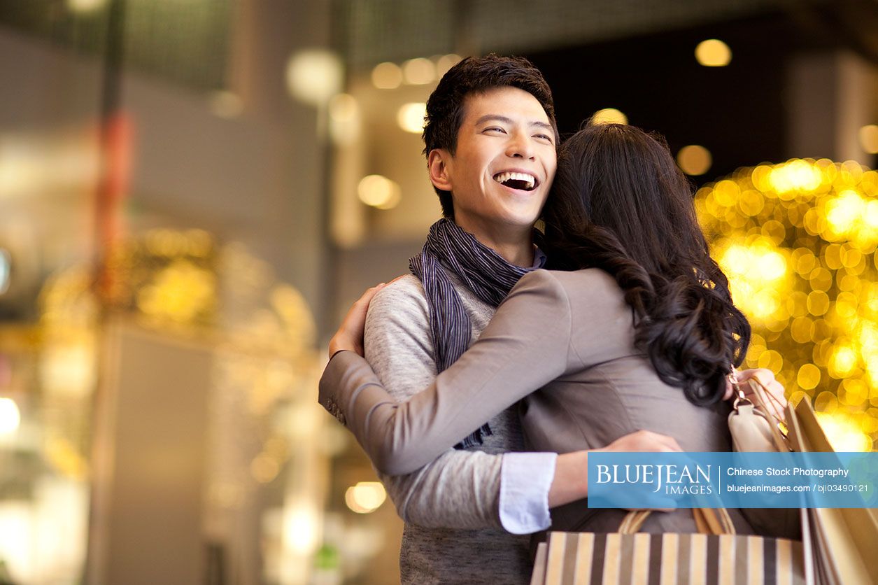 sweet-young-chinese-couple-embracing-with-shopping-bags-in-hands-high