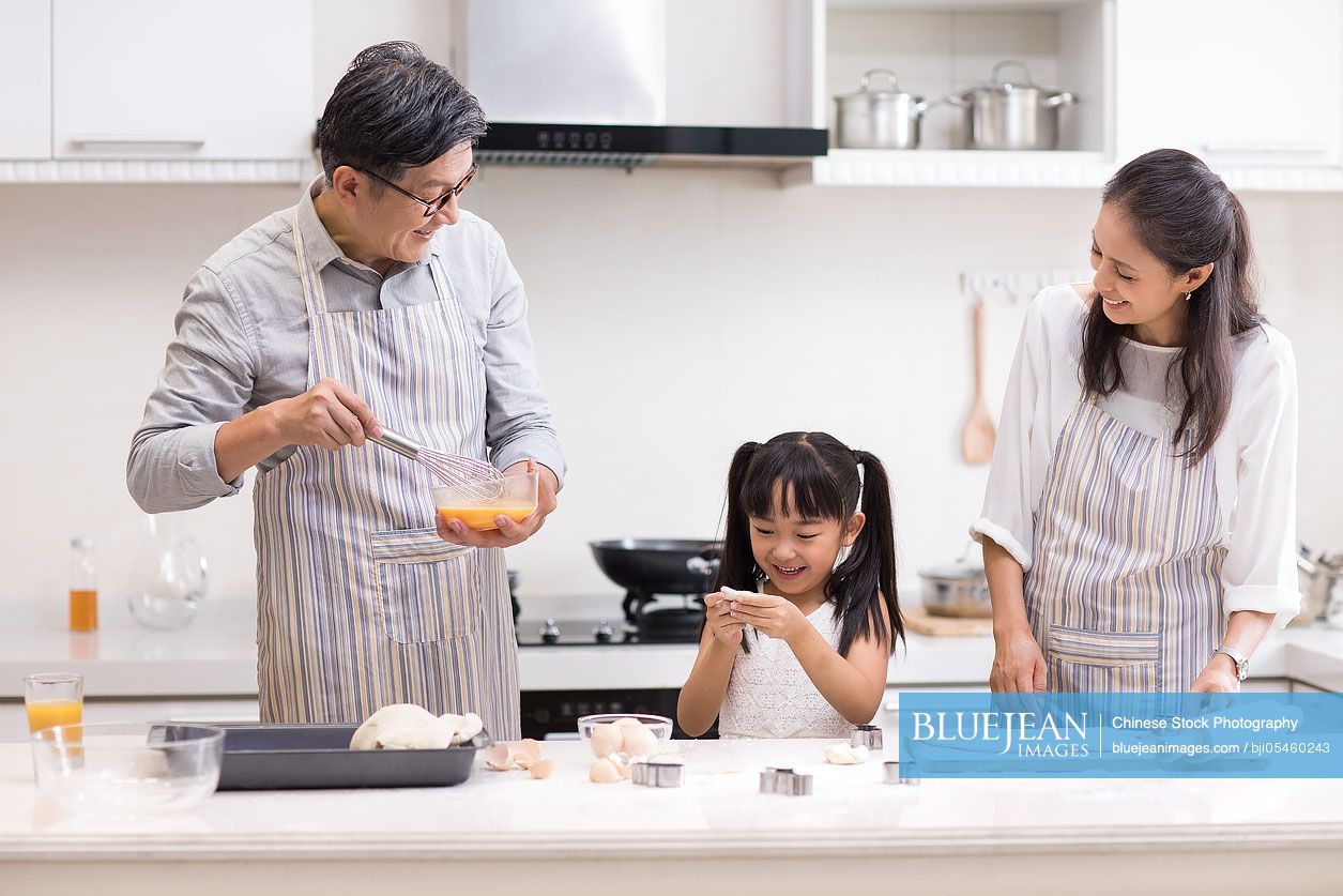 Happy little Chinese girl and grandparents baking cookies in kitchen