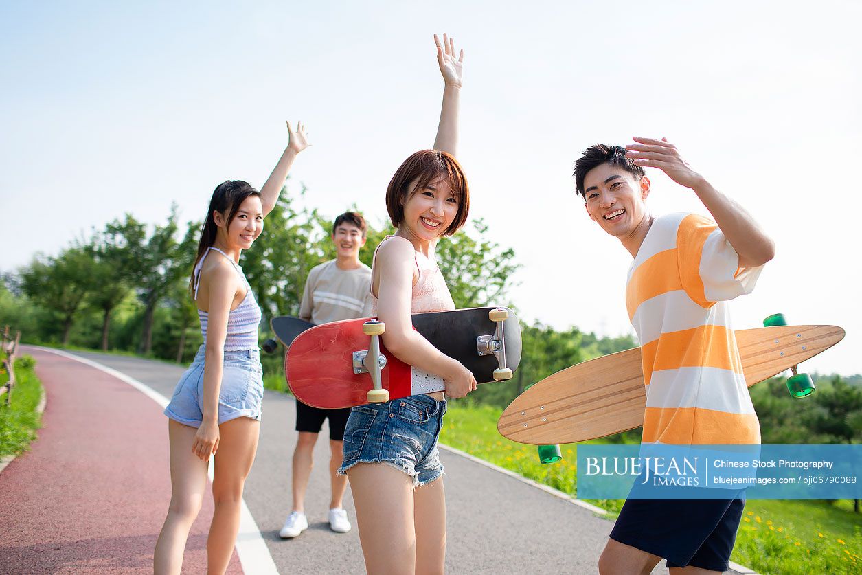 Happy young Chinese friends holding skateboards in park