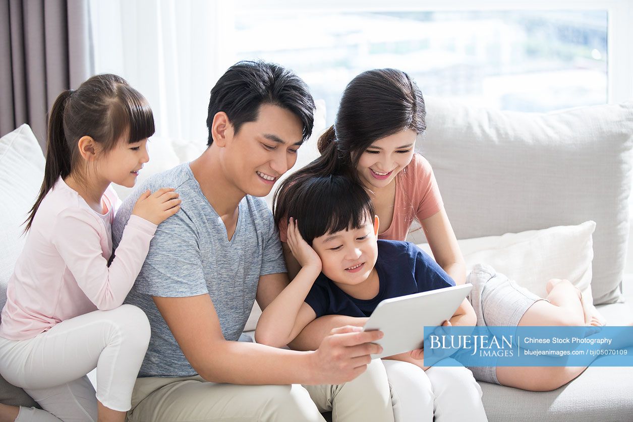 Happy young Chinese family using digital tablet at home