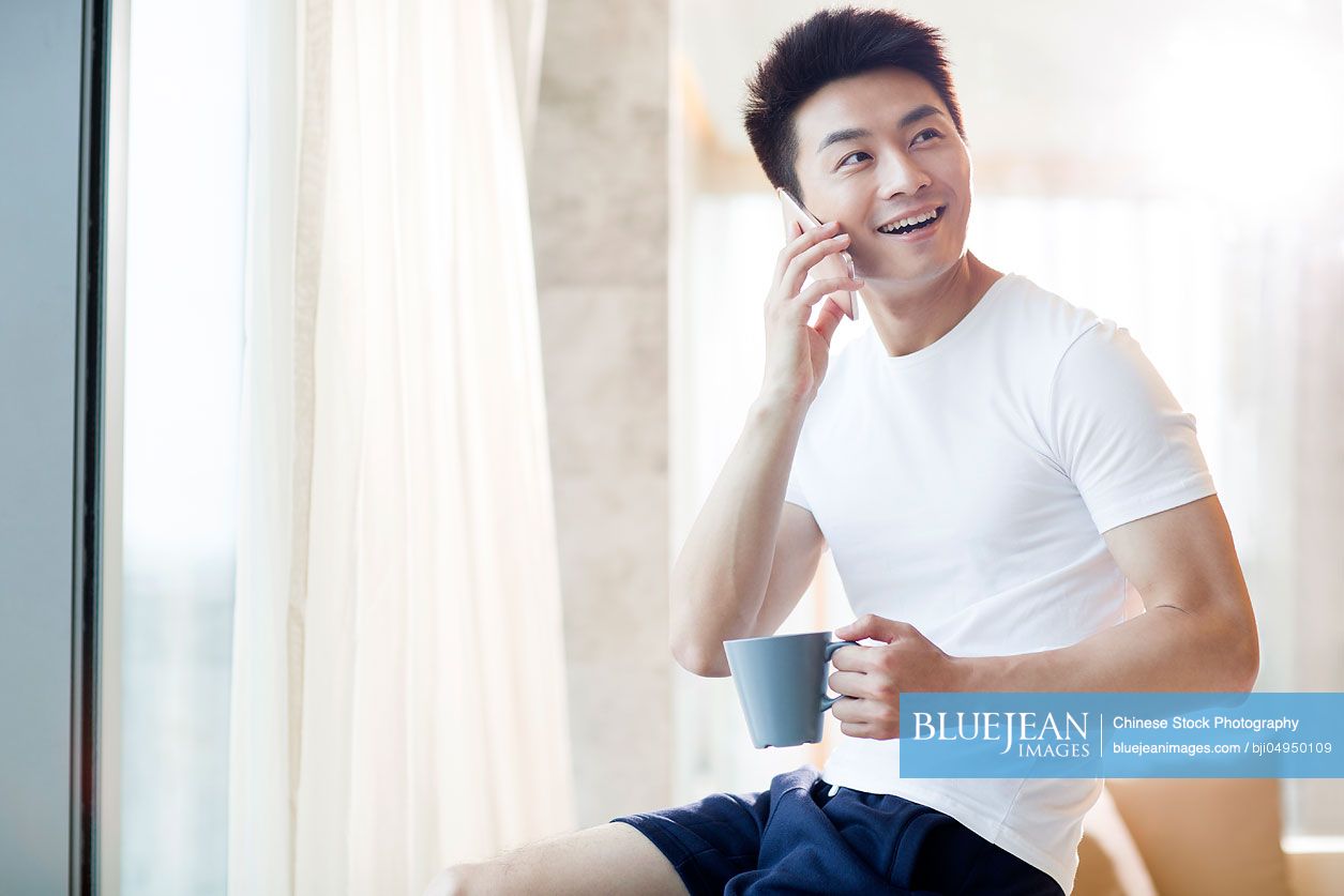 Young Chinese man talking on cell phone at home