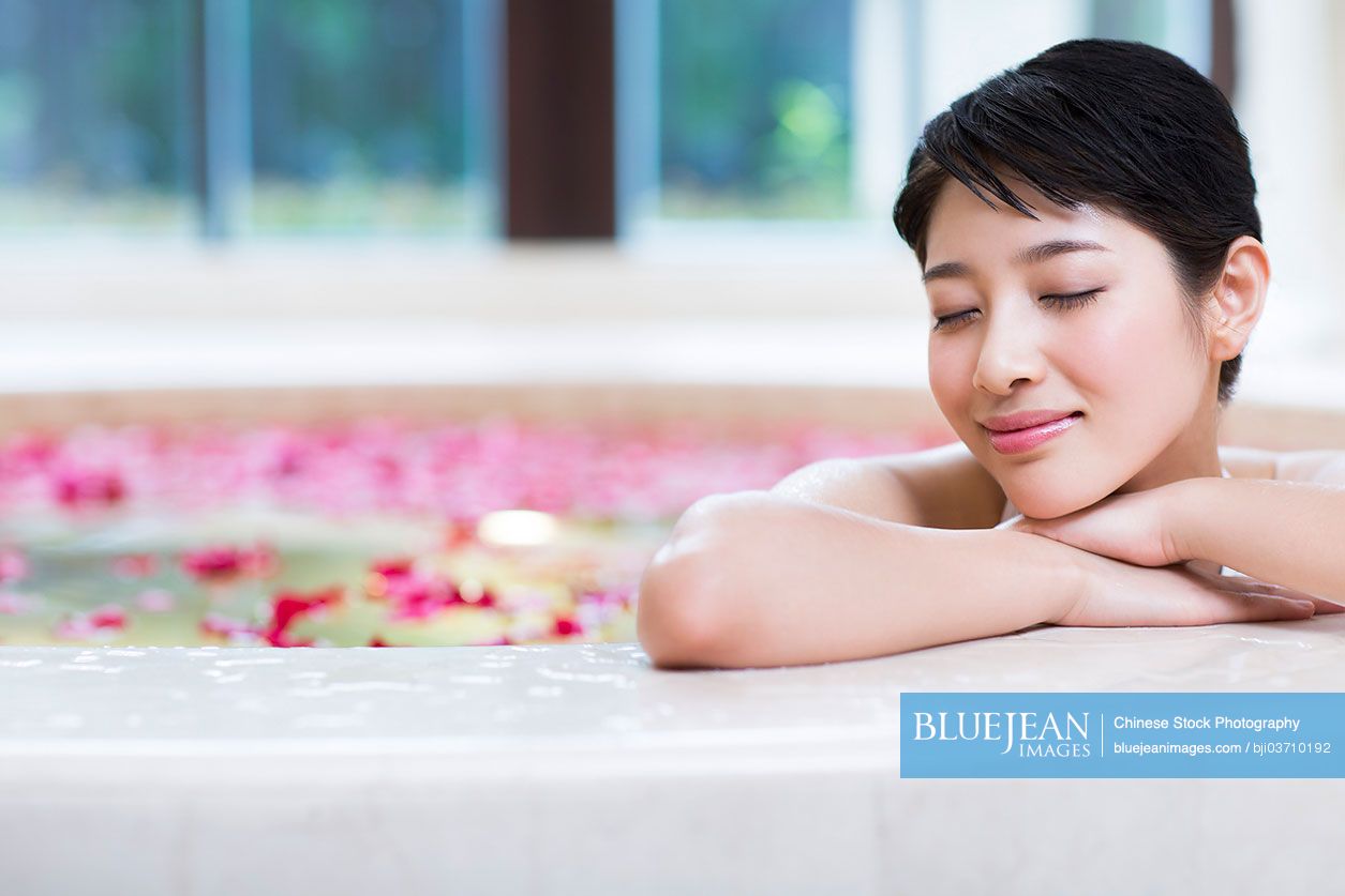 Beautiful young Chinese woman in bathtub with rose petals