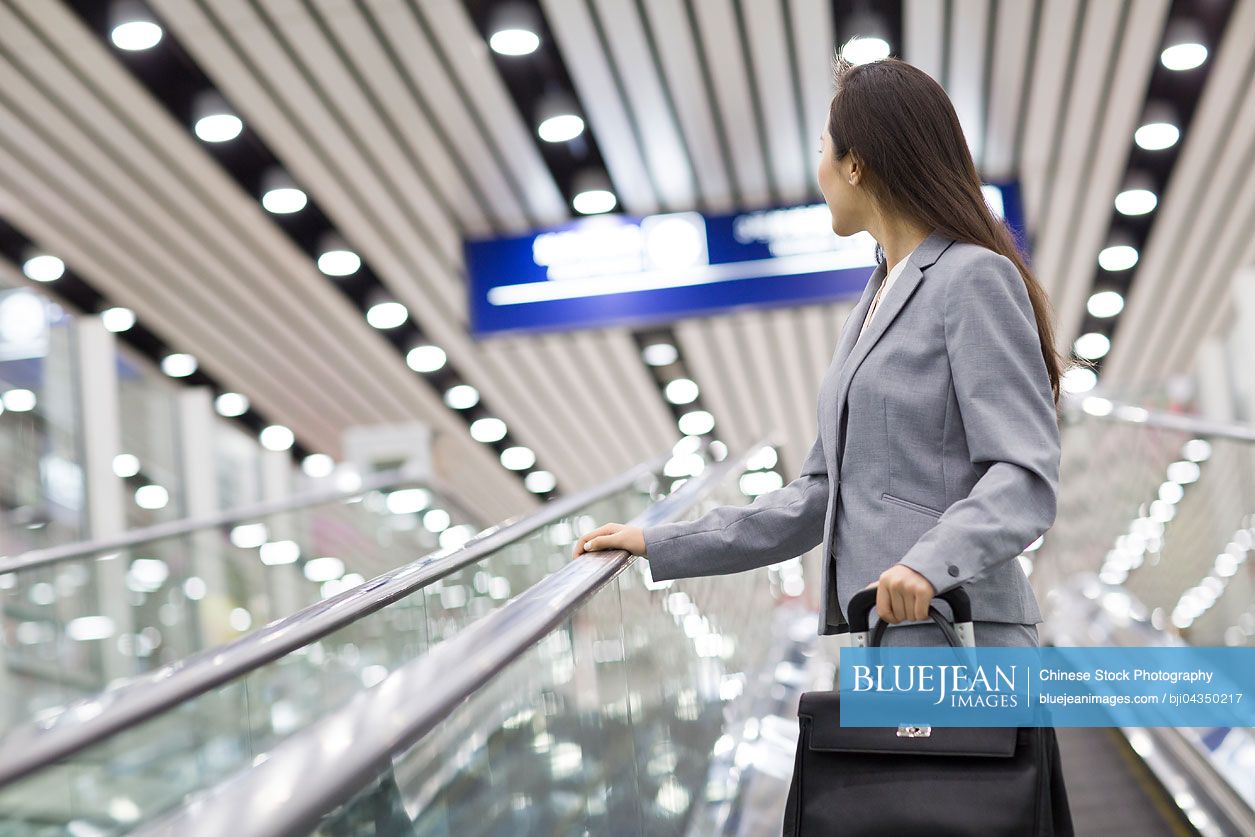 Young Chinese businesswoman with suitcase on escalator
