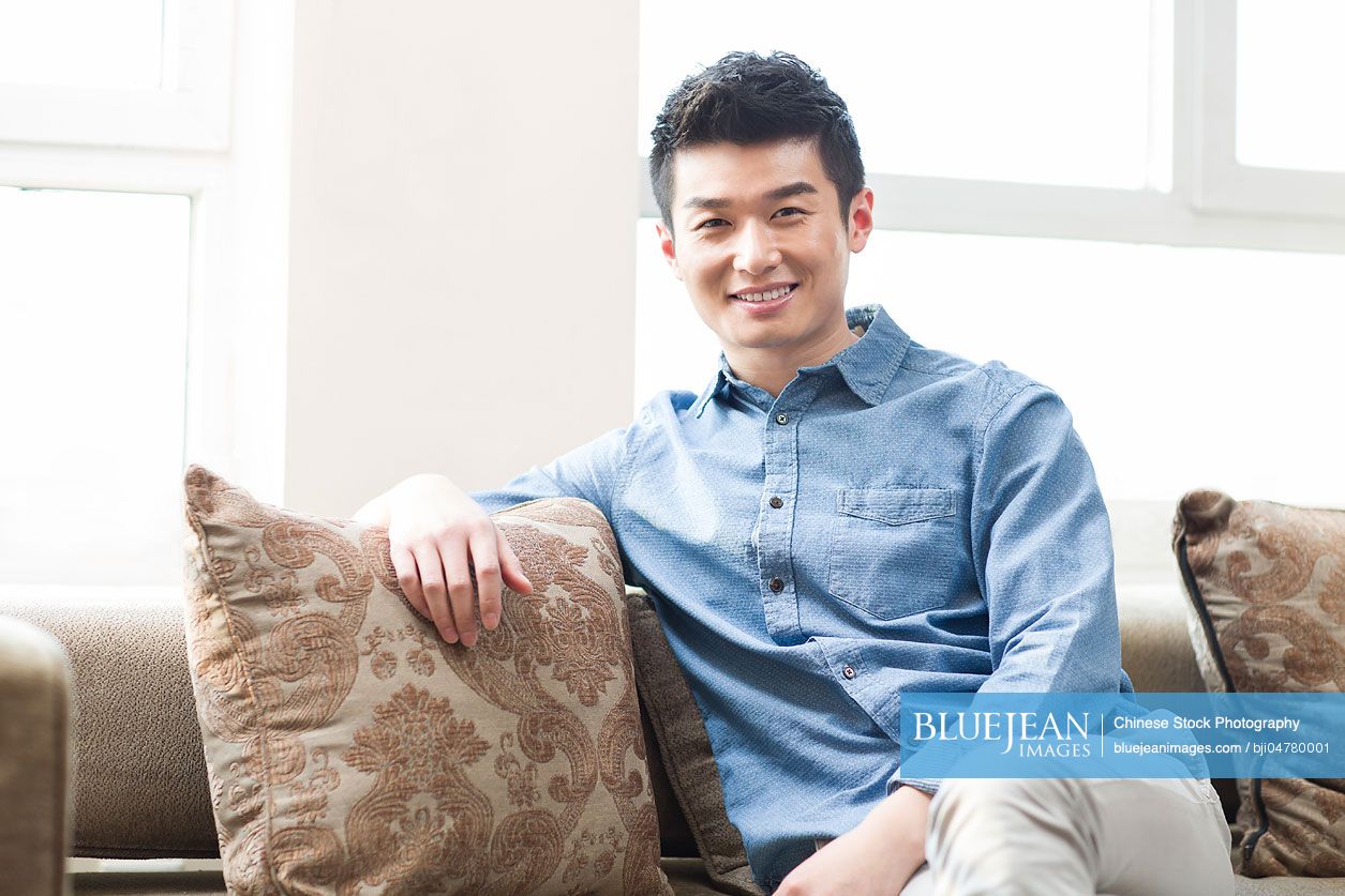 Happy young Chinese man resting in sofa