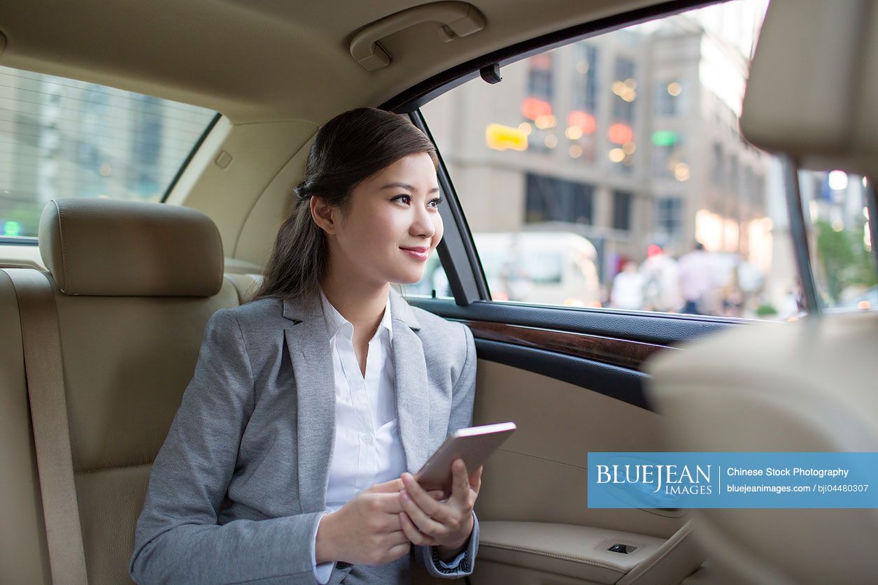 Chinese businesswoman holding smart phone in car back seat