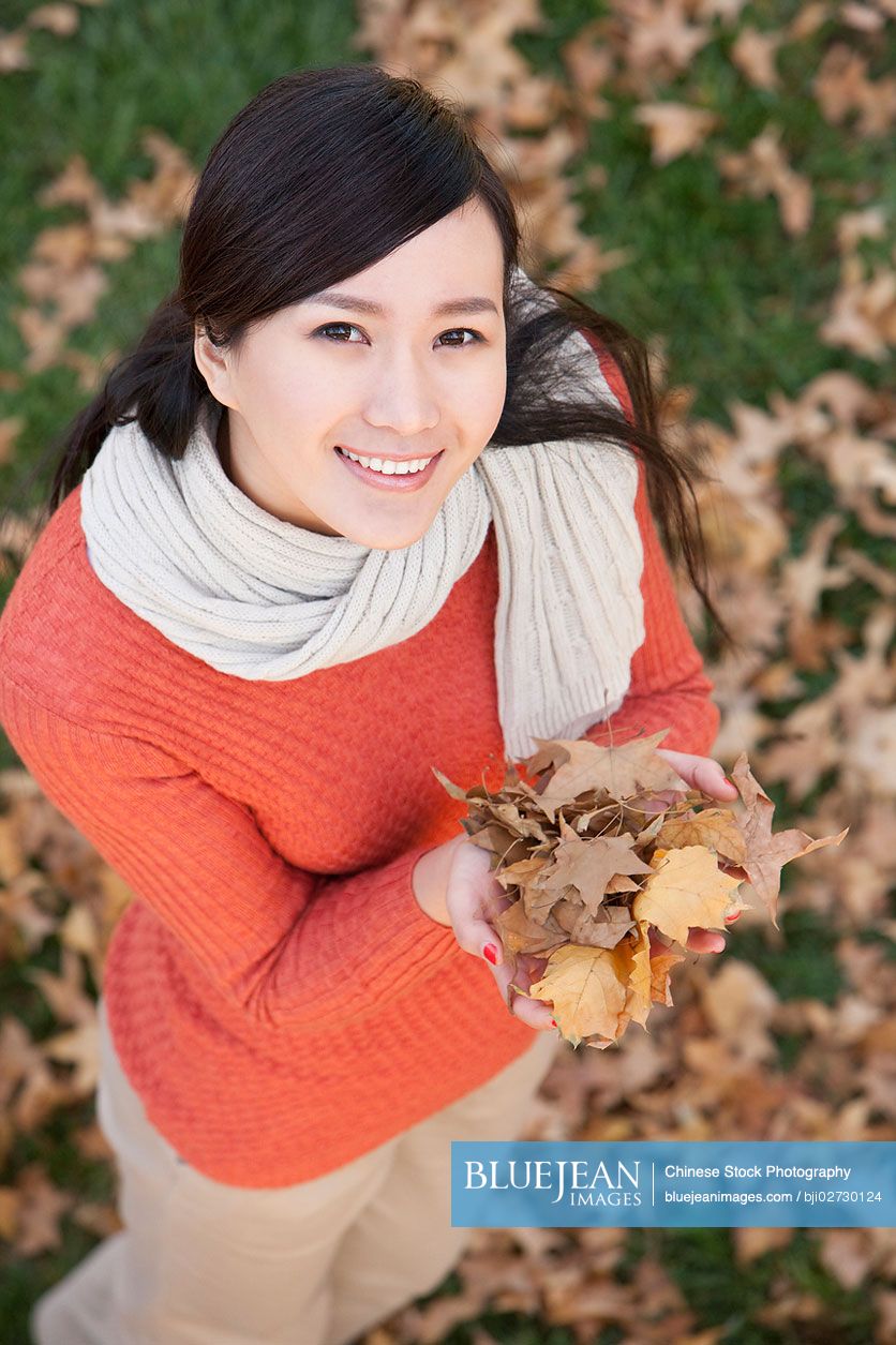 Young Chinese woman holding up autumn leaves