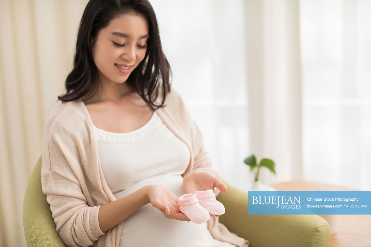 Cheerful Chinese pregnant woman holding baby socks