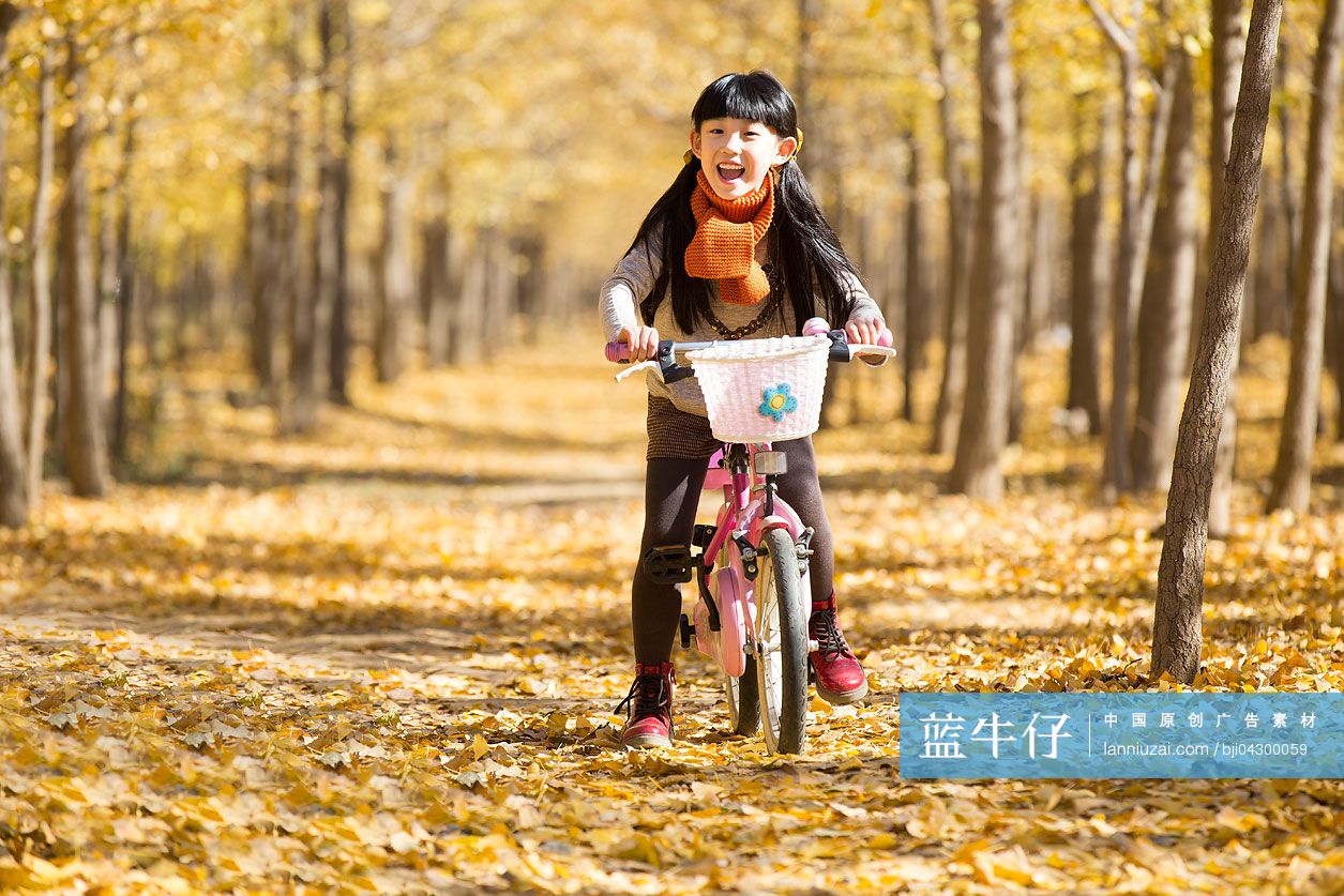 小女孩在秋日的树林里骑自行车