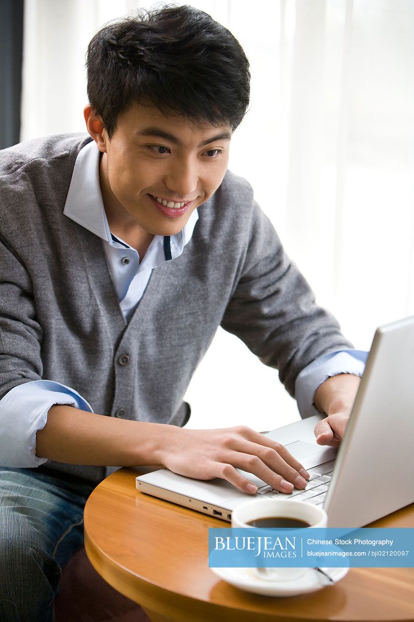 Smiling Chinese man using laptop at a coffee shop