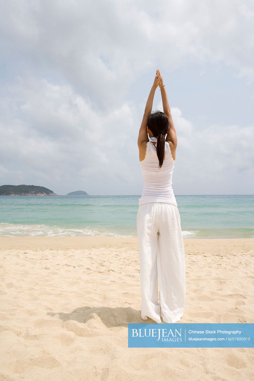 Young Chinese woman doing yoga on the beach