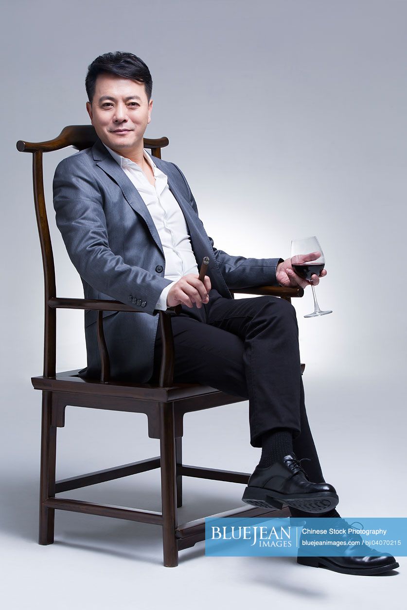 Mature Chinese businessman enjoying cigar and wine