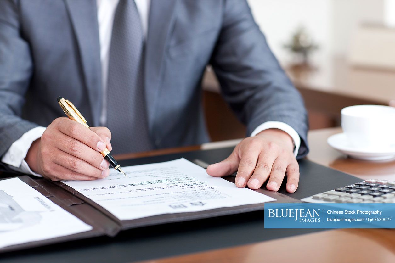 Chinese businessman signing a document in office