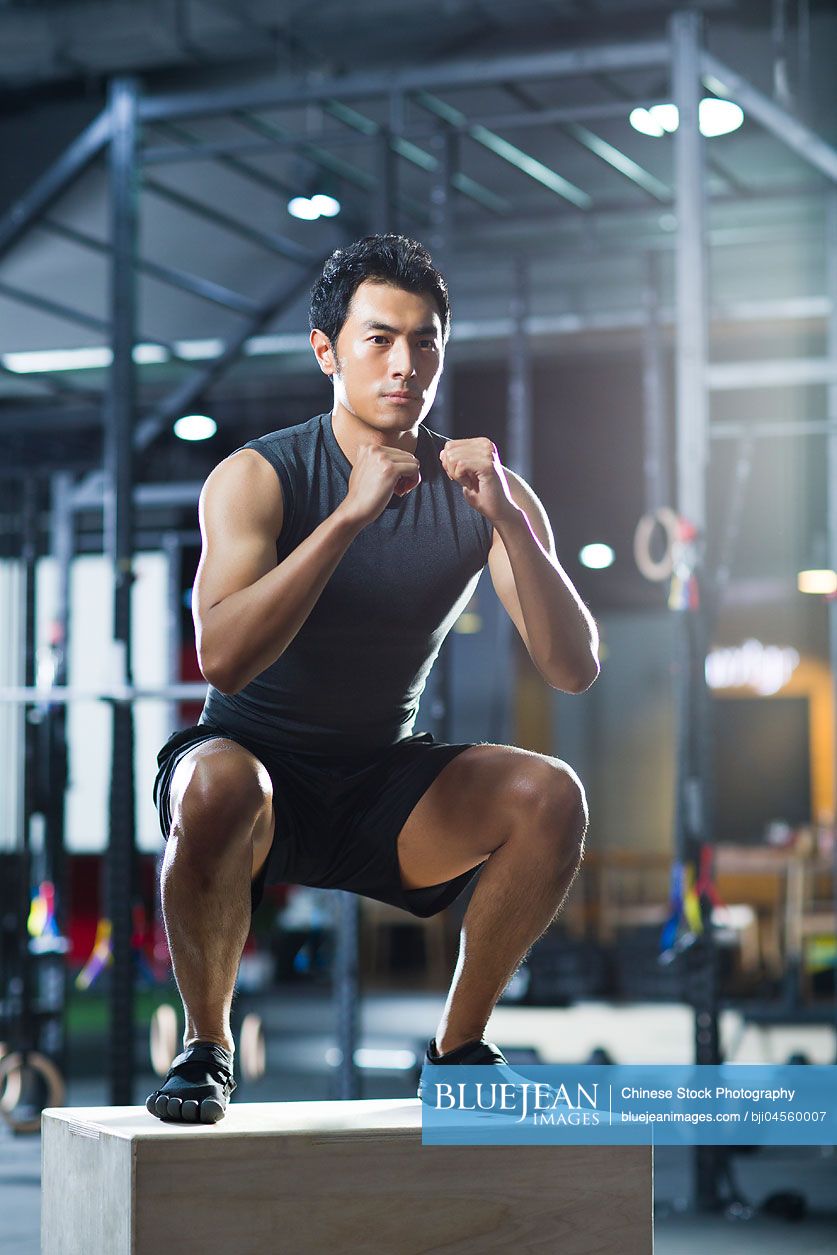 Young Chinese man doing box jump in crossfit gym