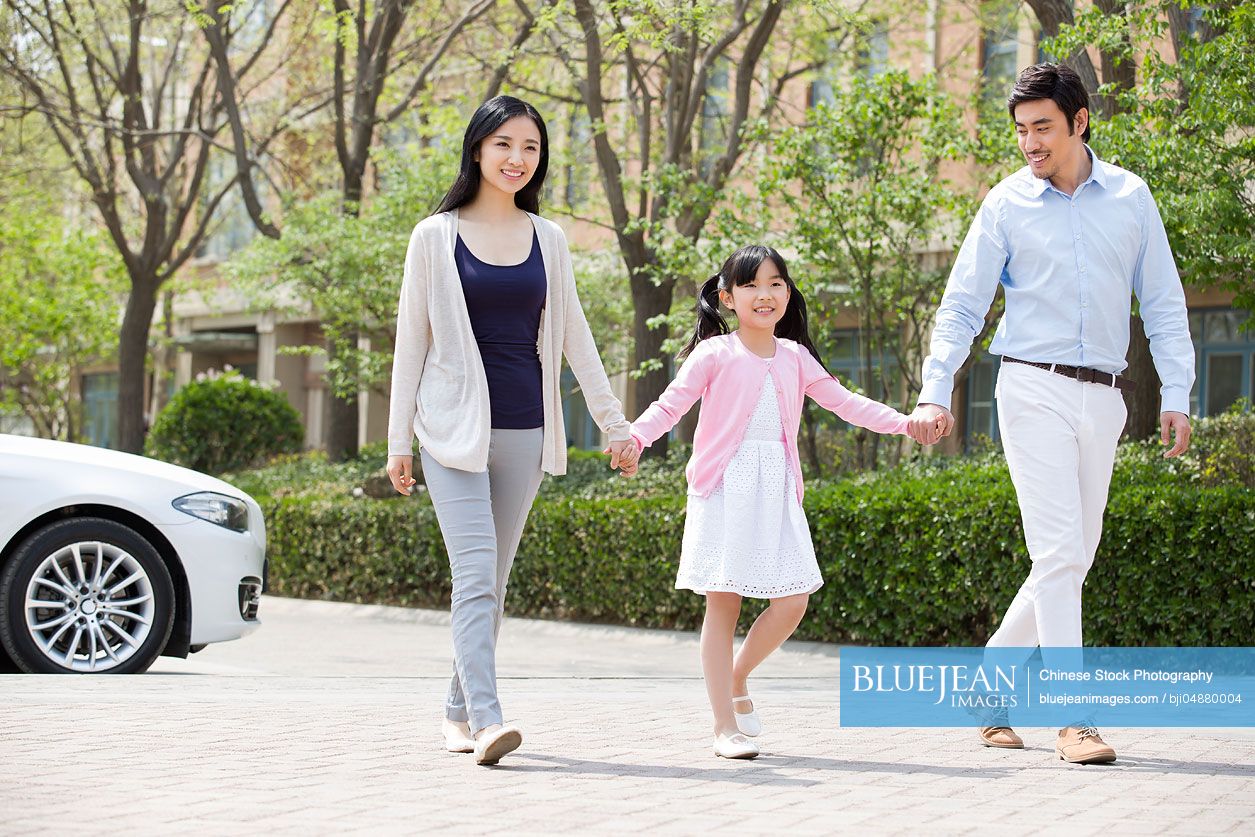 Happy young Chinese family holding hands walking