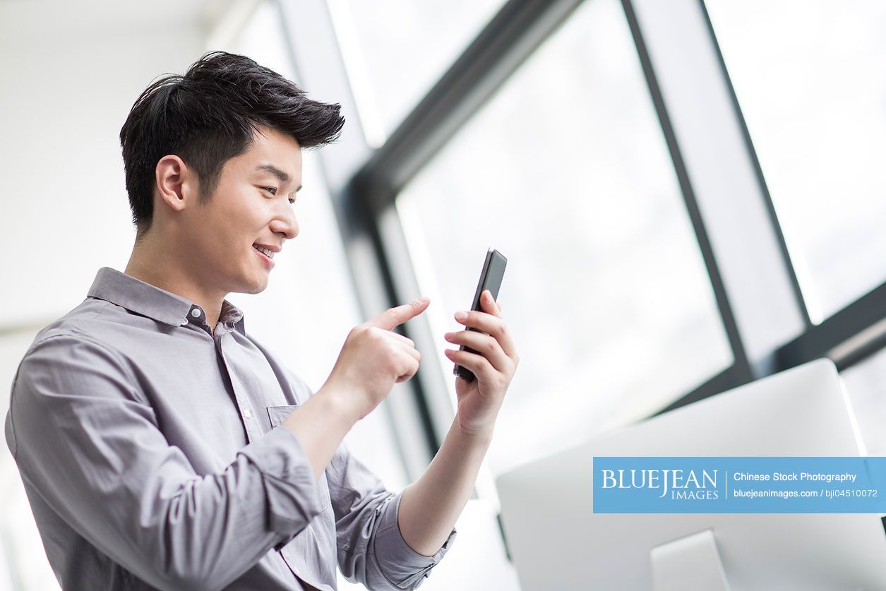 Young Chinese businessman using smart phone in office