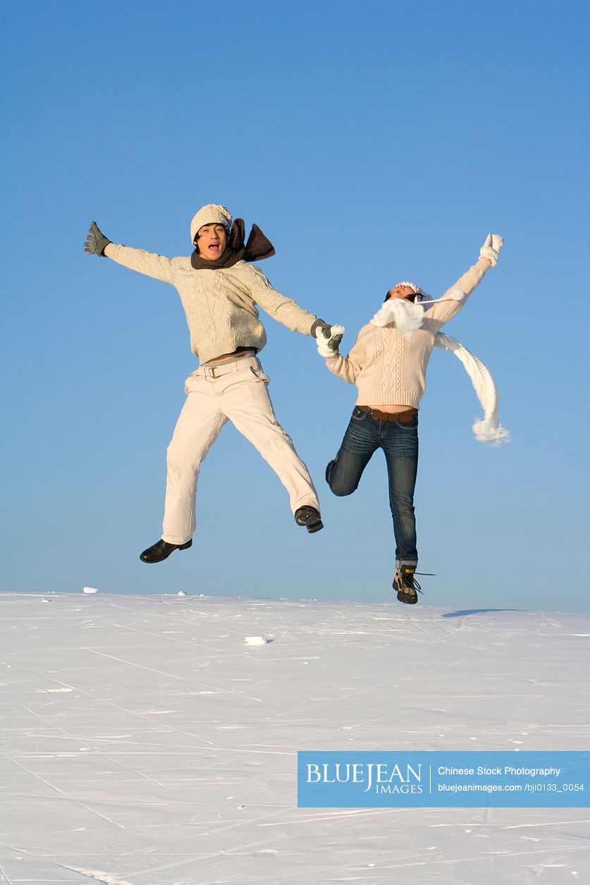 Young Chinese man and young Chinese woman jumping over a snowy landscape