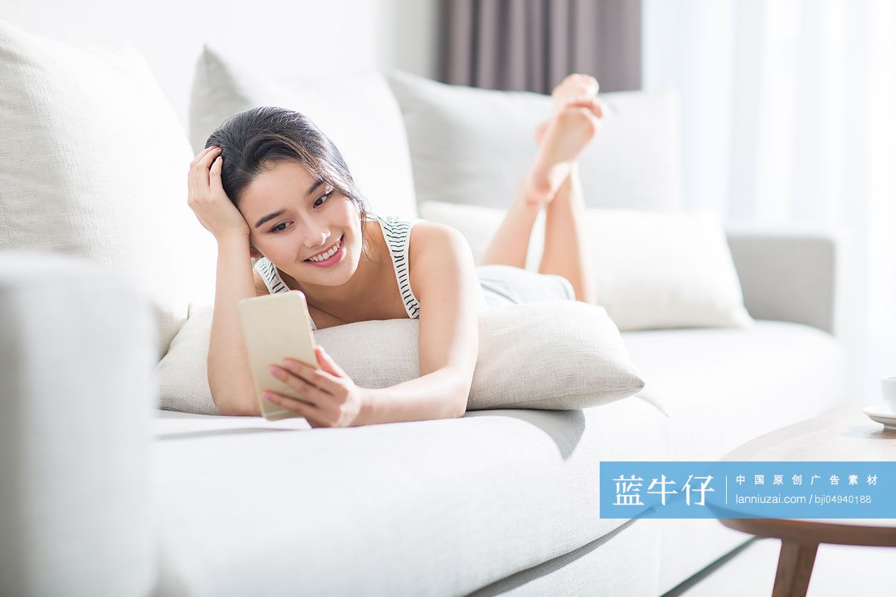 年轻女子趴在沙发上玩手机