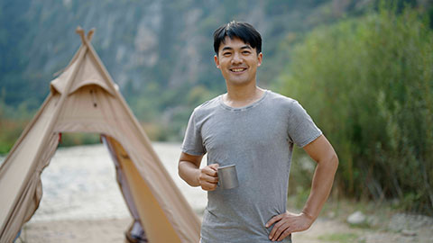 Happy young Chinese man camping outdoors