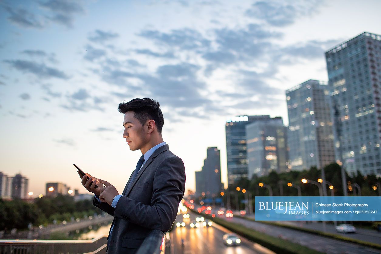 Confident young Chinese businessman using smart phone