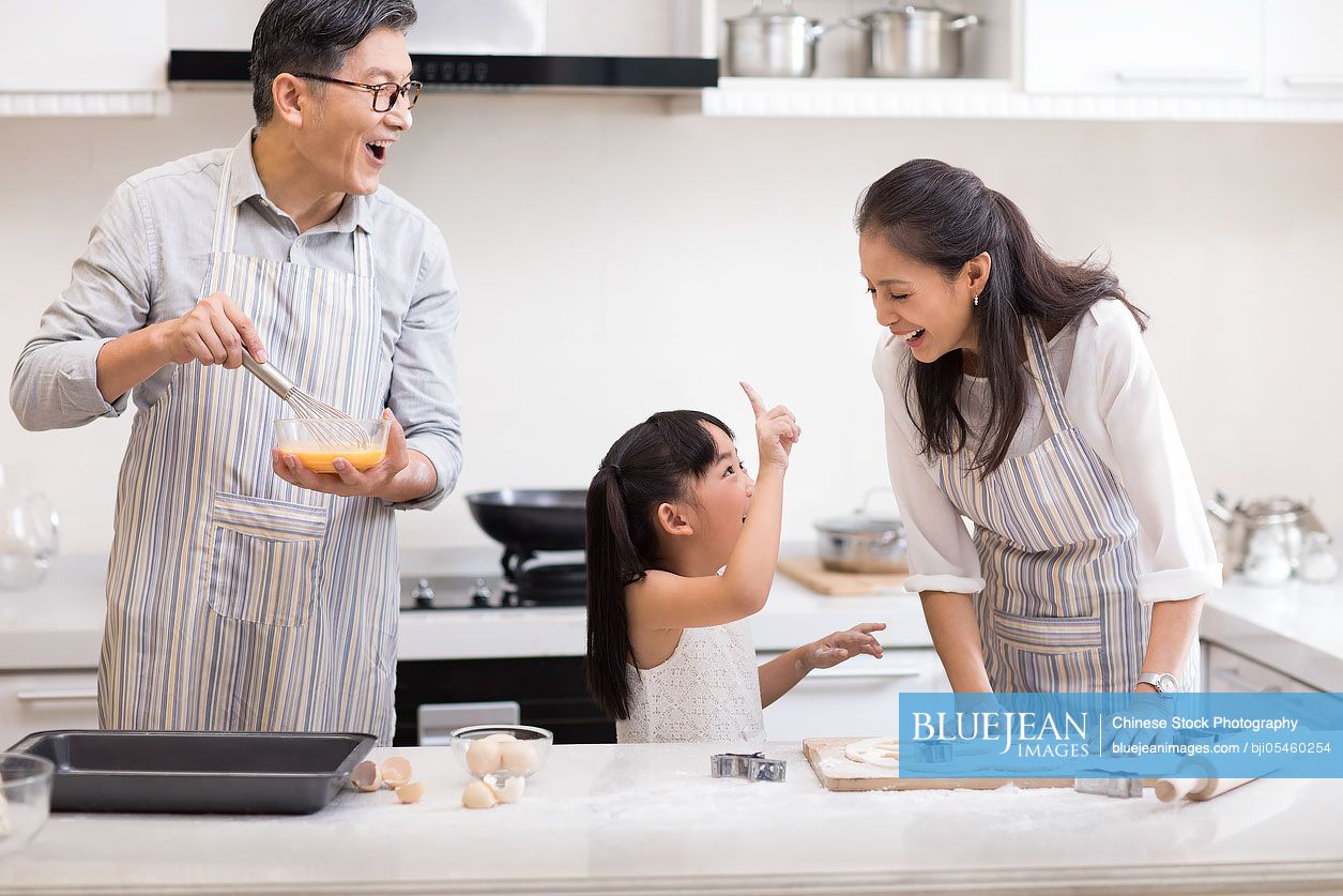 Happy little Chinese girl and grandparents baking cookies in kitchen