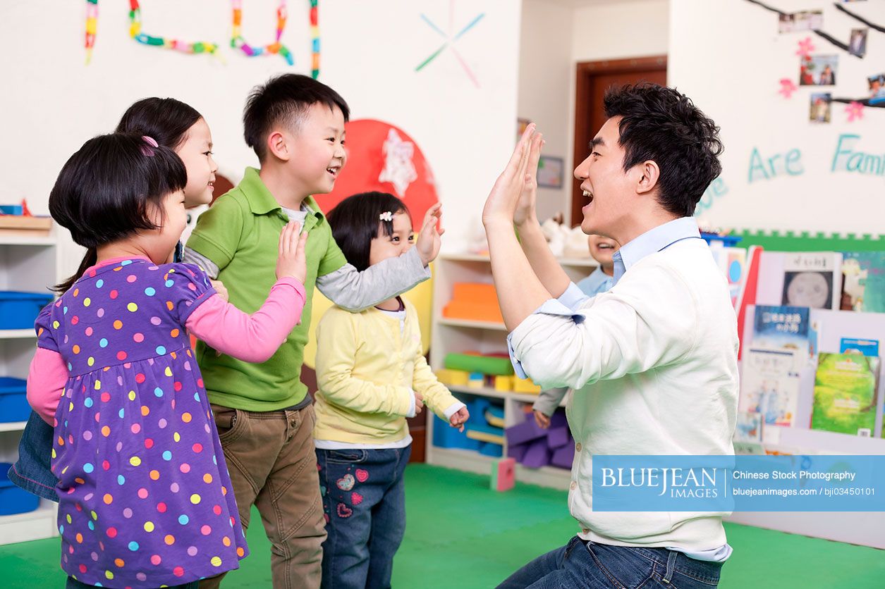 Happy Chinese kindergarten children playing clapping game with teacher