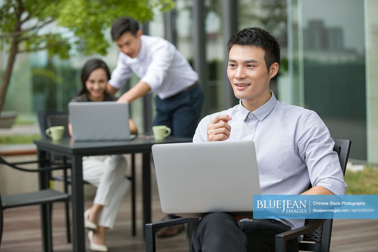 Young Chinese businessman using laptop outdoors