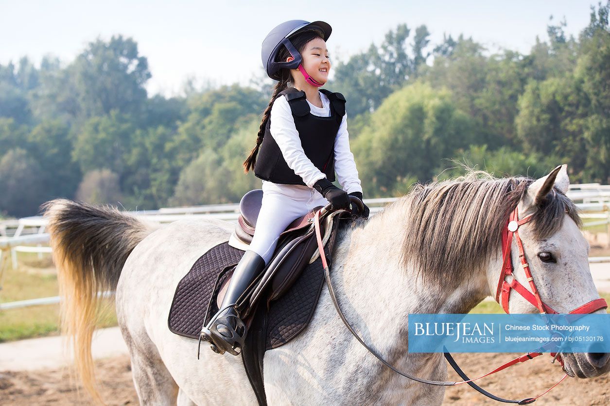 Cheerful little Chinese girl riding horse