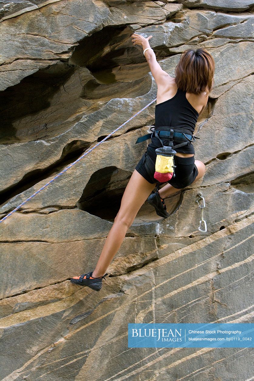 Young Chinese woman climbing rock